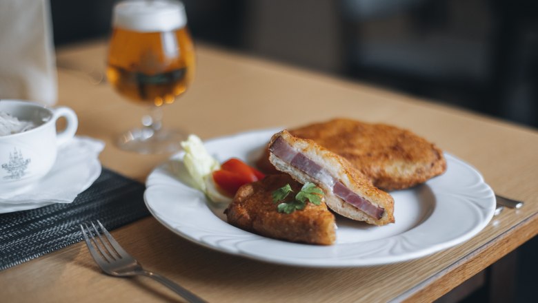 Schweinsschopf im Erdäpfelmantel, © Niederösterreich Werbung/David Schreiber Ein Teller mit Schweinsschopf im Erdäpfelmantel, serviert mit Salat und einem Glas Bier im Hintergrund.