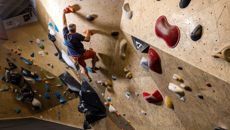 BigWall Bouldering, © BigWall Bouldering Person beim Bouldern an einer Kletterwand mit bunten Griffen.