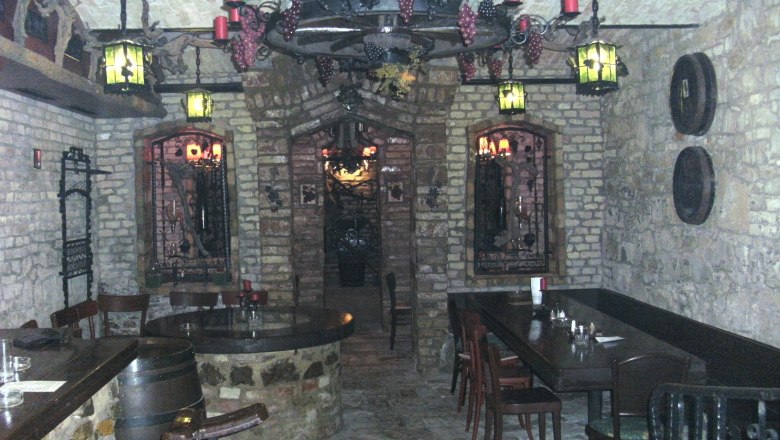 Heurigenlokal im Keller, © Burgherrenrestaurant Ein rustikales Heurigenlokal im Keller mit Steinwänden, Holzmöbeln und dekorativen Lichtern.