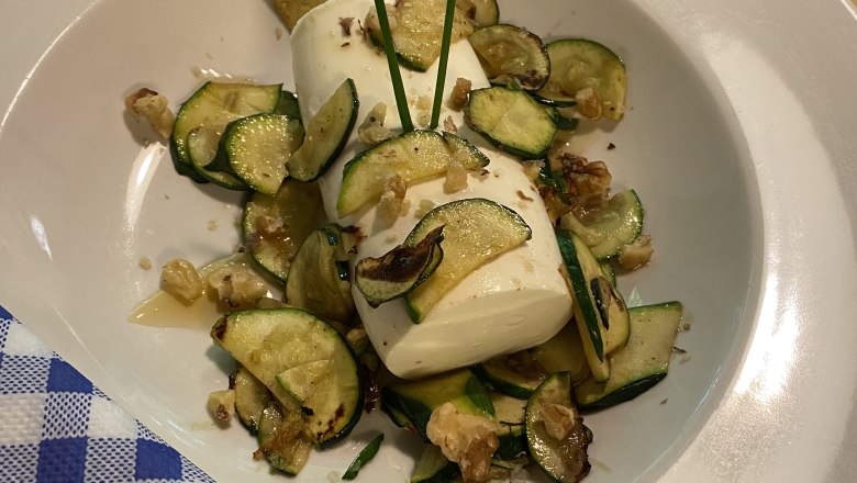 TD-Alpenvereinshaus Tulln-Teller, © Birgit Rabacher Ein Teller mit Zucchinischeiben, Mozzarella und Walnüssen, dekoriert mit Schnittlauch, auf einem Holztisch mit blau-weiß kariertem Servietten.