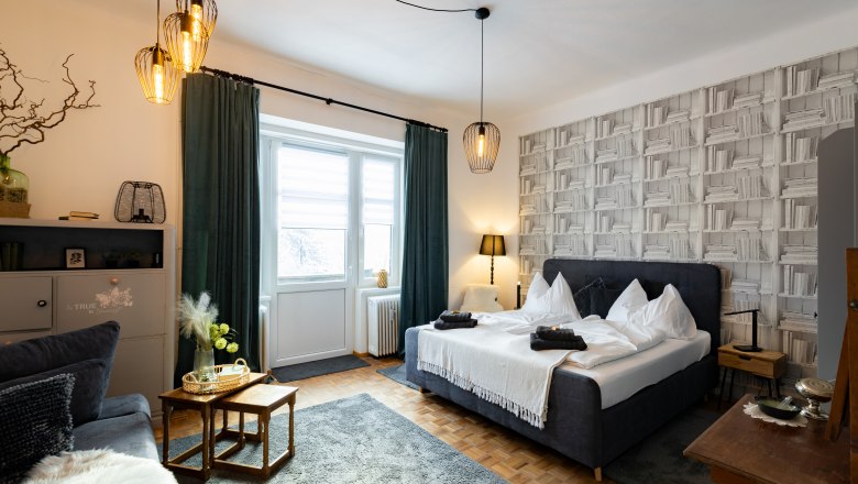 Apartment 1, © Atelier Fürtner-Ton Gemütliches Schlafzimmer mit Doppelbett, dekorativen Lampen und Bücherregal-Tapete.