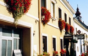 haus, © Gasthof Weinknecht Ein traditionelles Gasthaus mit gelber Fassade und roten Blumen an den Fenstern.