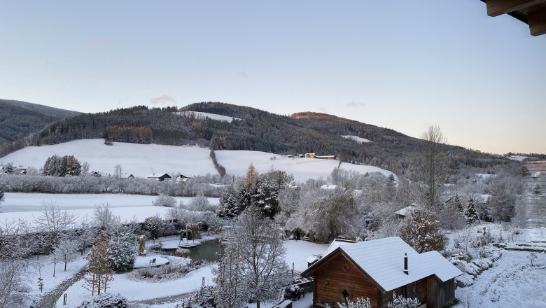 Ausblick Molzbachhof, © Peter Pichler Winterlandschaft mit schneebedeckten Hügeln und einem Holzhaus im Vordergrund.