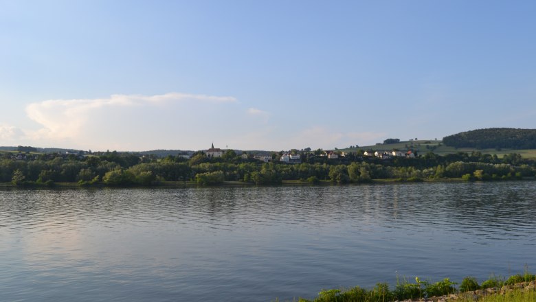 Außenansicht5, © Gasthof Donaublick Landschaft mit Fluss, Hügeln und Dorf im Hintergrund bei klarem Himmel.