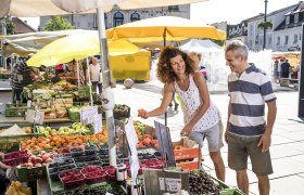 Tullner Naschmarkt, © Stadtgemeinde Tulln, Robert Herbst Menschen kaufen Obst auf einem Markt mit gelben Sonnenschirmen.