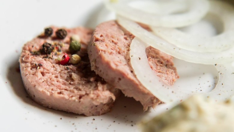 Heurigenjause, © Weinberghof Ilkerl Nahaufnahme von Wurstscheiben mit Pfefferkörnern und Zwiebelringen auf einem Teller.