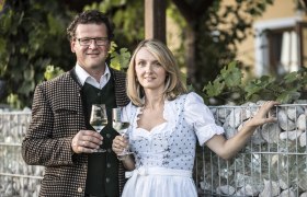 Sonja und Markus Oßberger, © Nino Zimmerhackl Ein Mann und eine Frau in traditioneller Kleidung halten Weingläser in der Hand.
