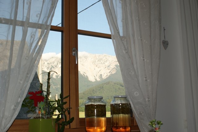 Ferienwohnung Schneebergblick, © Familie Zwinz Blick aus einem Fenster mit Vorhängen auf einen Berg. Zwei Gläser mit Flüssigkeit stehen auf der Fensterbank.