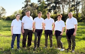 Familie Haidl, © Familie Haidl Sechs Personen in weißen Polohemden stehen auf einer Wiese vor Bäumen.