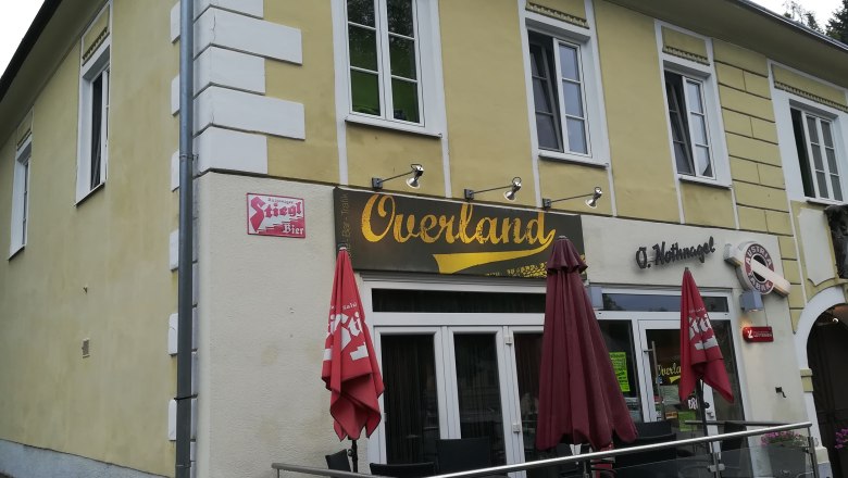 Overland, © Wiener Alpen Gelbes Gebäude mit dem Schriftzug 'Overland' und roten Sonnenschirmen.