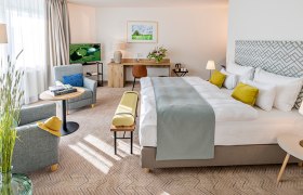 Golfresort Haugschlag, © by Haugschlag Modernes Hotelzimmer mit großem Bett, Sitzbereich und Schreibtisch.