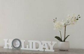 Herzlich Willkommen, © Multimedia Lauda Dekoration mit Schriftzug 'HOLIDAY' und weißer Orchidee in einem Topf auf einem Tisch.