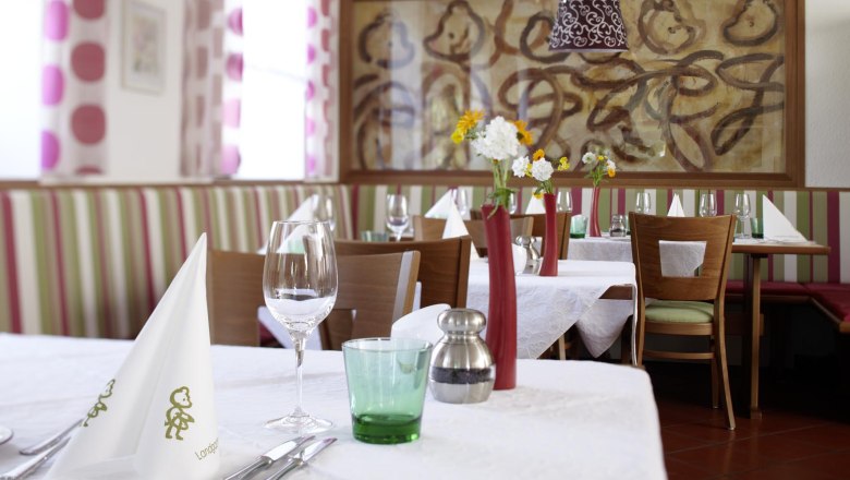 Gasthof Bärenwirt, © Crepaz Innenansicht eines stilvoll gedeckten Restaurants mit weißen Tischdecken, Blumenvasen und Kunst an der Wand.