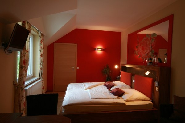 Geniesserzimmer, © Rosenhotel Gemütliches Schlafzimmer mit roter Wand und Doppelbett.