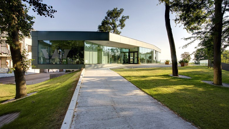 Gebeitsvinothek Weritas in Kirchberg am Wagram, © Gemeinde Kirchberg am Wagram Moderne Glasfassade der Gebietsvinothek Weritas in Kirchberg am Wagram, umgeben von Bäumen und gepflegtem Rasen.