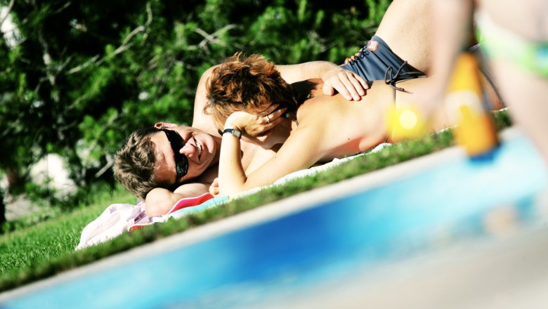 Faulenzen auf der Liegewiese, © weinfranz.at Ein Paar liegt entspannt auf einer Wiese neben einem Pool.