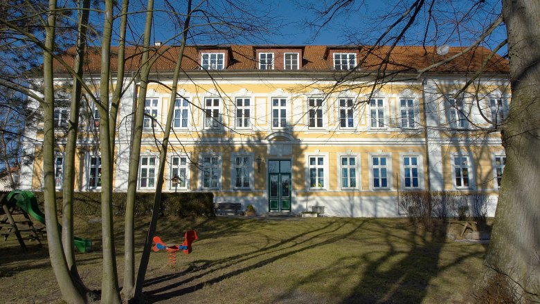 Gemeinde Golling an der Erlauf, © zVg Gemeinde Golling an der Erlauf Gelbes Gebäude mit weißen Fensterrahmen und rotem Dach, umgeben von Bäumen und Spielplatz.
