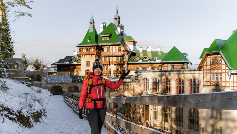 Villen und -Palasthotels am winterlichen Semmering erwandern, © Luxusgämsen Person in Winterkleidung vor einem großen Gebäude mit grünen Dächern im Schnee.