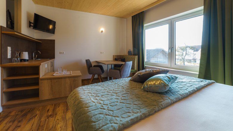 Muehlbachzimmer, © Maria Harrauer Gemütliches Hotelzimmer mit Holzboden, Doppelbett, kleinem Tisch und Stühlen, Fernseher und großem Fenster mit Ausblick.