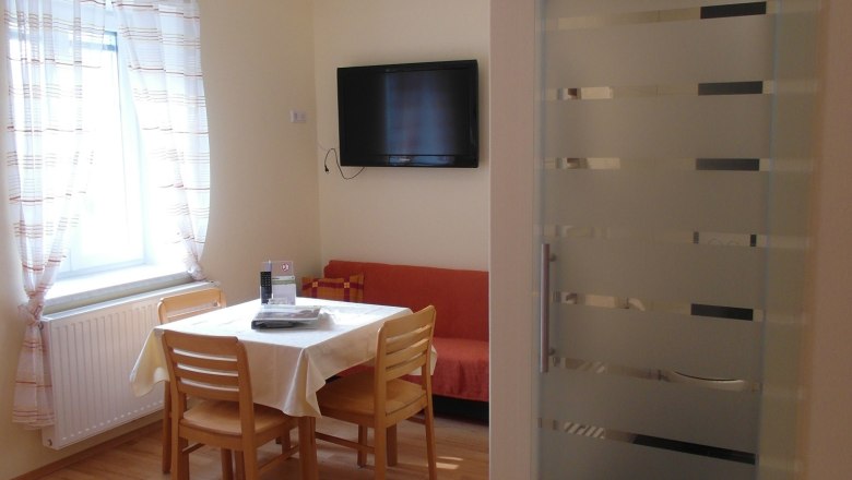 Essecke im Zimmer am Lugerhof, © Lugerhof Helles Zimmer mit Essecke, Tisch, Stühlen, Bett und Flachbildfernseher.