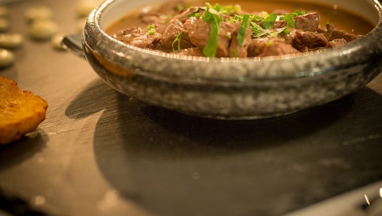 Restaurant - Lammragout, © Schlossschenke Ein Schokovulkan-Dessert auf einer Schieferplatte mit einer Kugel Eis und roten Rosenblättern dekoriert.