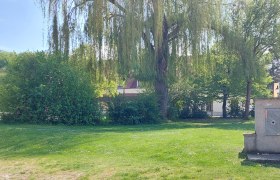 Zeltplatz Loosdorf, © Gemeinde Fallbach Grüne Wiese mit Bäumen und einem kleinen Gebäude im Hintergrund.