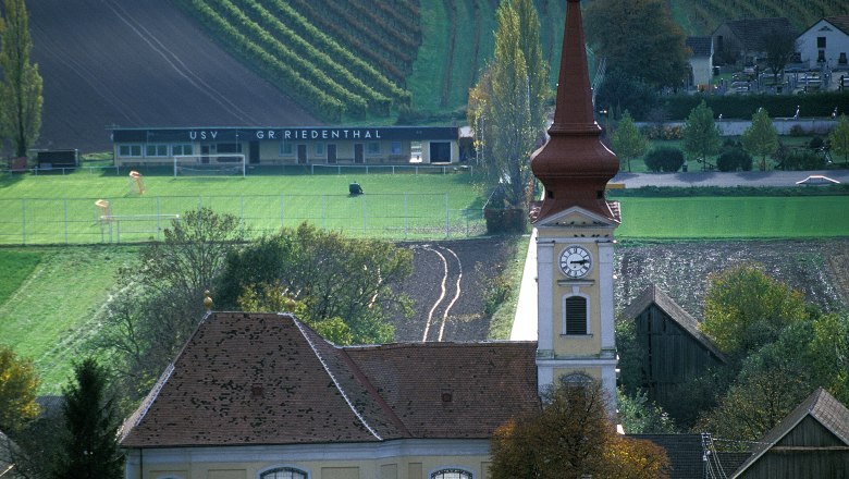 Pfarrkirche Großriedenthal, © Donau Niederösterreich Pfarrkirche Großriedenthal mit Kirchturm und umliegenden Feldern und Gebäuden.