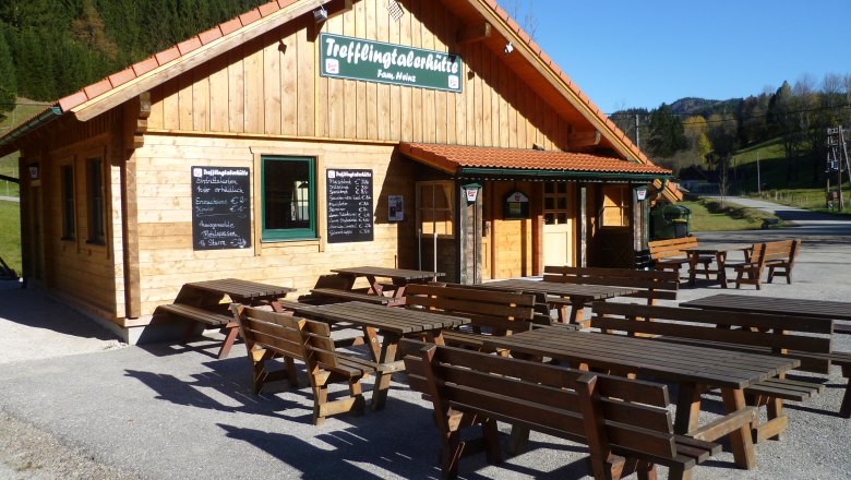 Trefflingtalerhütte, © zVg Holzhütte mit Tischen im Freien, sonniger Tag.