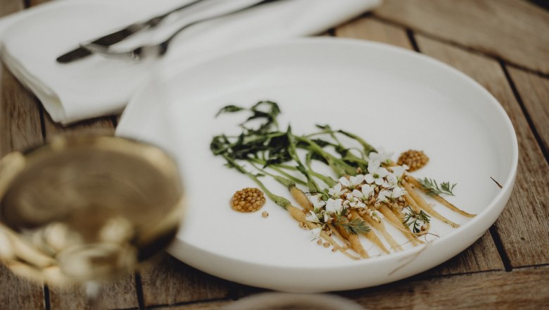 Neues bei Chef’s Table oder Triad privat, © Niederösterreich Werbung/Sophie Menegaldo Elegantes Gericht mit Gemüse und Blüten auf einem weißen Teller.