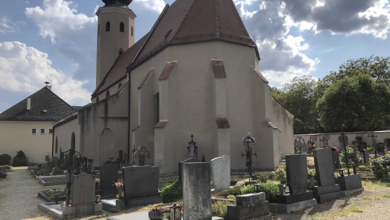 aggsbach-markt-kirche2, © Donau NÖ Tourismus Kirche mit Friedhof und Grabsteinen im Vordergrund, bewölkter Himmel.