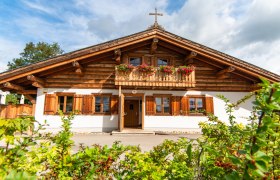 Kaminstubn Schwechat Mannswörth, © Kaminstubn Traditionelles Holzhaus mit Balkon und Blumenkästen, blauer Himmel im Hintergrund.