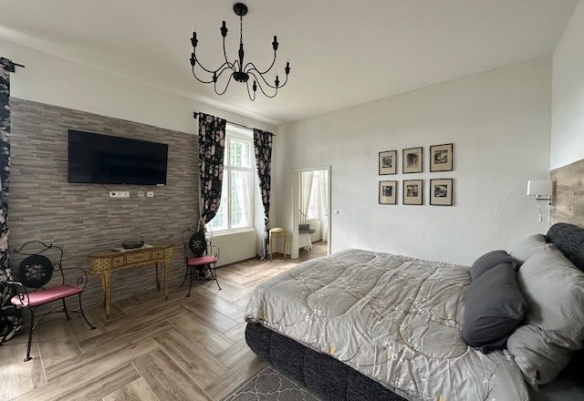 Zimmer Deluxe, © Schloss Gut Ziegersberg Elegantes Hotelzimmer mit großem Bett, Kronleuchter, Fernseher und dekorativen Elementen.