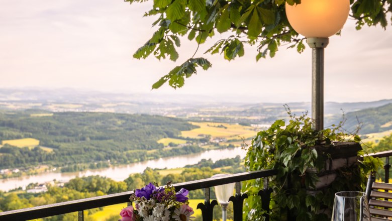 Hotel Schachner, © Niederösterreich Werbung / Maximilian Pawlikowsky Terrasse mit Tisch, Blumen und Blick auf Flusslandschaft.