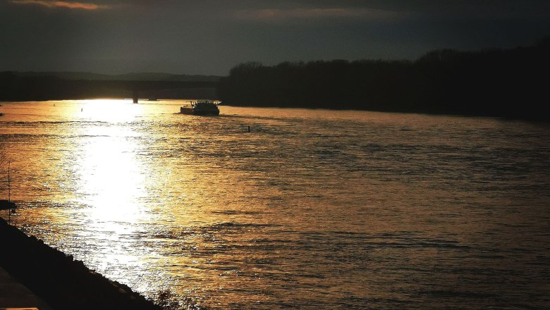 Sonnenuntergang vorm Campingplatz, © Szilágyi Sonnenuntergang über einem Fluss mit einem Boot und dunklen Wolken am Himmel.