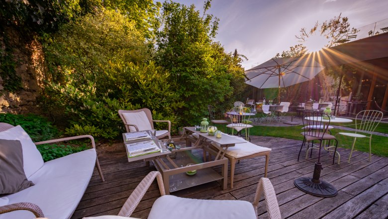 Hotel Landhaus Moserhof, © Niederösterreich Werbung / Maximilian Pawlikowsky Gemütliche Terrasse mit Sitzmöbeln und Sonnenschirmen im Garten eines Hotels.