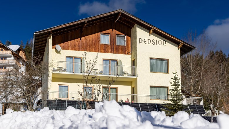 zweistöckiges Gebäude mit der Aufschrift "Pension", Solapanelen und Schnee vor dem Haus, © Pension Klug zweistöckiges Gebäude mit der Aufschrift "Pension", Solapanelen und Schnee vor dem Haus, © Pension Klug