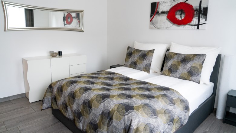 Schlafzimmer, © Martin Zekar Modernes Schlafzimmer mit Doppelbett, abstraktem Kunstwerk und Spiegel.