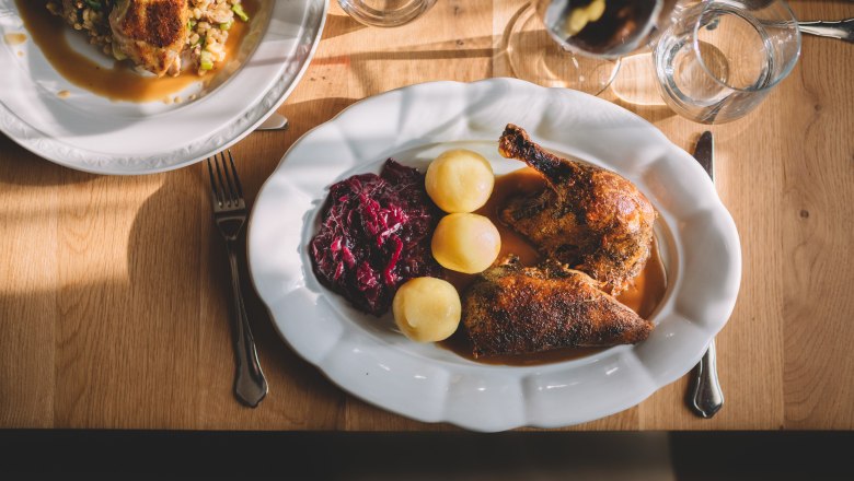 Ofenfrische Bauernente, © Niederösterreich Werbung/Mara Hohla Ein Teller mit gebratener Ente, Rotkohl und Kartoffeln auf einem Holztisch.