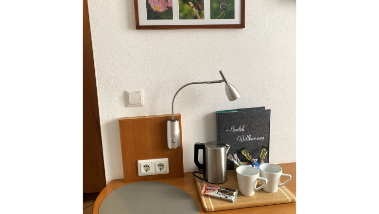Zimmer, © Trachsler Ein Tisch mit Wasserkocher, zwei Tassen, Snacks und einem Willkommensheft. An der Wand hängen drei Naturfotos.
