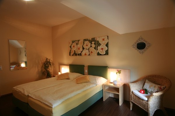 Nostalgiezimmer, © Rosenhotel Gemütliches Schlafzimmer mit Doppelbett, Rattan-Sessel, Nachttisch und Blumenbild an der Wand.