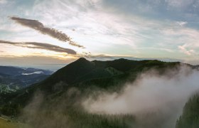 Wanderung Sonnenaufgang, © Semmering Hirschenkogel Panoramablick auf den Sonnwendstein bei Sonnenaufgang mit Nebel und einem Aussichtsturm im Vordergrund.