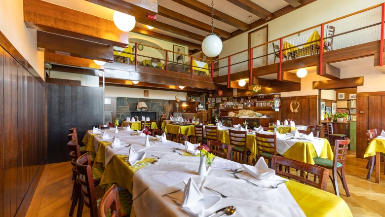 Gemütliches Ambiente im Looshaus, © Wiener Alpen / Christian Kremsl Innenansicht eines gemütlichen Restaurants mit Holzbalken, gedeckten Tischen und einer Galerie.