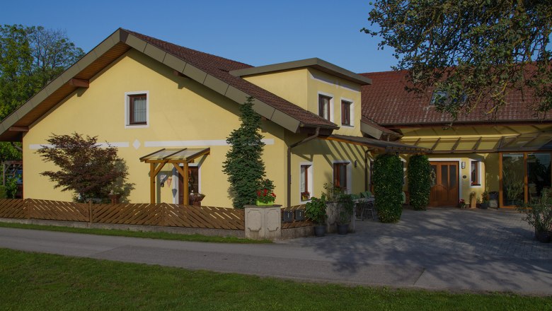 Hausansicht, © Privatzimmer Leeb Gelbes Einfamilienhaus mit rotem Dach und Garten.