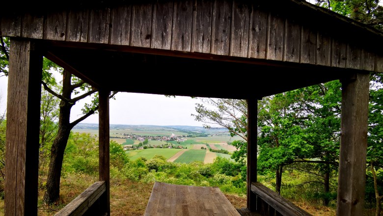 Hollenstein Aussichtswarte, © Weinstraße Weinviertel Holzhütte mit Blick auf Felder und Dorf in der Ferne.