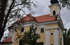 Maria Bründl Poysdorf, © Weinviertel Tourismus Gelbe Kirche mit rotem Dach und Turm, umgeben von Bäumen.