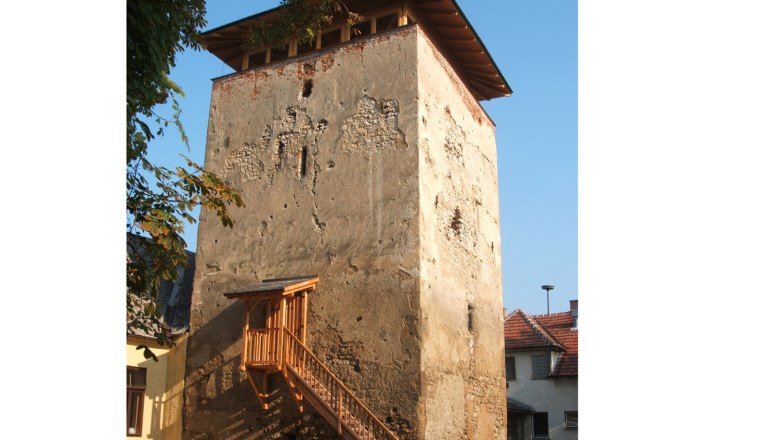 Wehrturm Palterndorf, © Herbert Nowohradsky Ein alter Wehrturm mit bröckelnder Fassade und einem hölzernen Treppenaufgang, umgeben von Häusern und Bäumen.