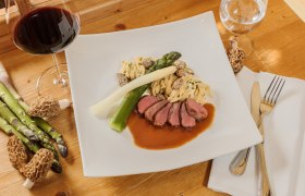 Kaiser von Österreich, © Rita Newman Gourmetgericht mit Fleisch, Spargel, Nudeln und Morcheln auf einem weißen Teller, daneben ein Glas Rotwein.