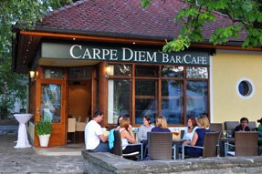 Carpe Diem_Außenansicht, © Carpe Diem Außenansicht eines Cafés mit dem Namen Carpe Diem, Menschen sitzen an Tischen im Freien.