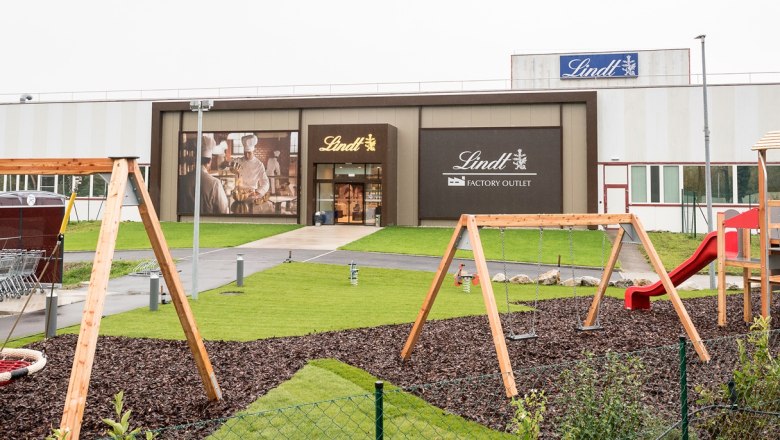playground, © Lindt & Sprüngli Spielplatz vor einem Lindt Factory Outlet mit Schaukeln und Rutsche.