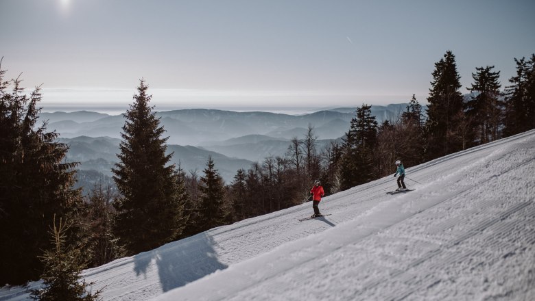 Schigebiet Unterberg, © Schigebiet Unterberg | katischweiger.fotography Zwei Skifahrer auf einer Piste im Schigebiet Unterberg mit Bergpanorama im Hintergrund.